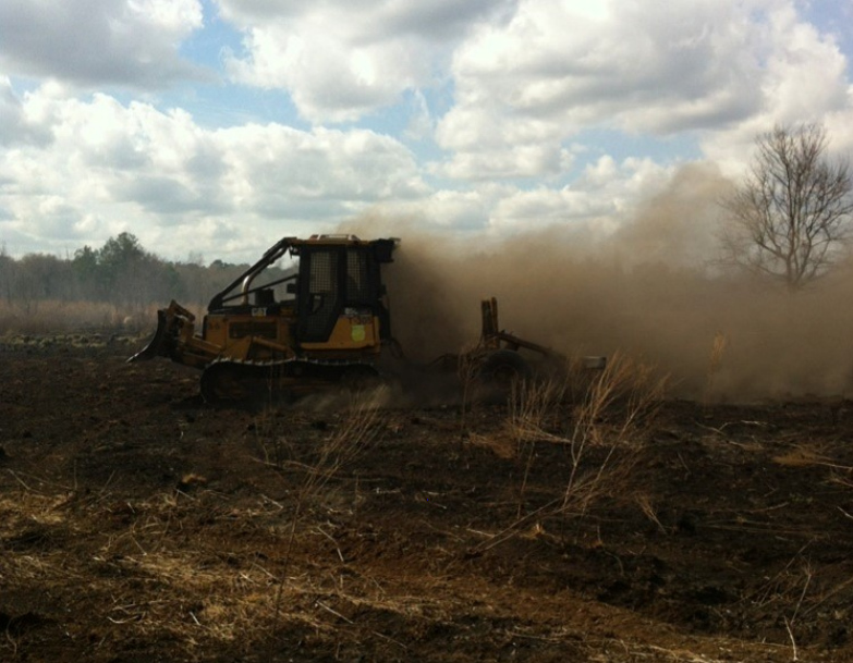 Photo of a bulldozer making several passes through thick muck to get down to then mineral soil.
