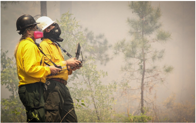 A smoke scientist working with an unmanned aerial vehicle researcher to collect samples from a prescribed fire smoke plume.